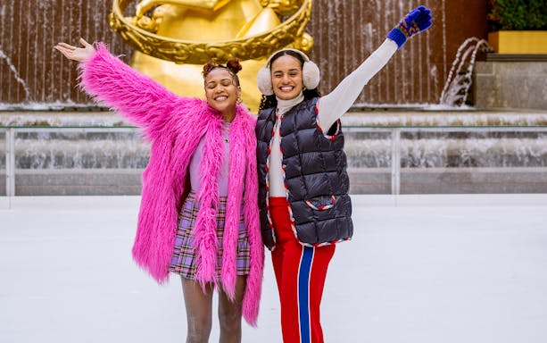 Two people ice skating at Rockefeller Center with Prometheus statue in the background.