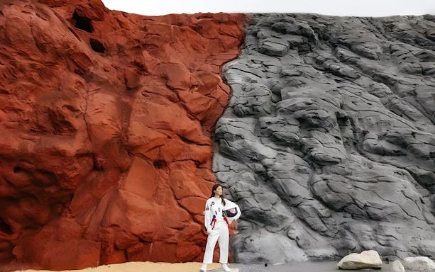 Person in astronaut suit standing by red and gray rock formations at LOF LAND.