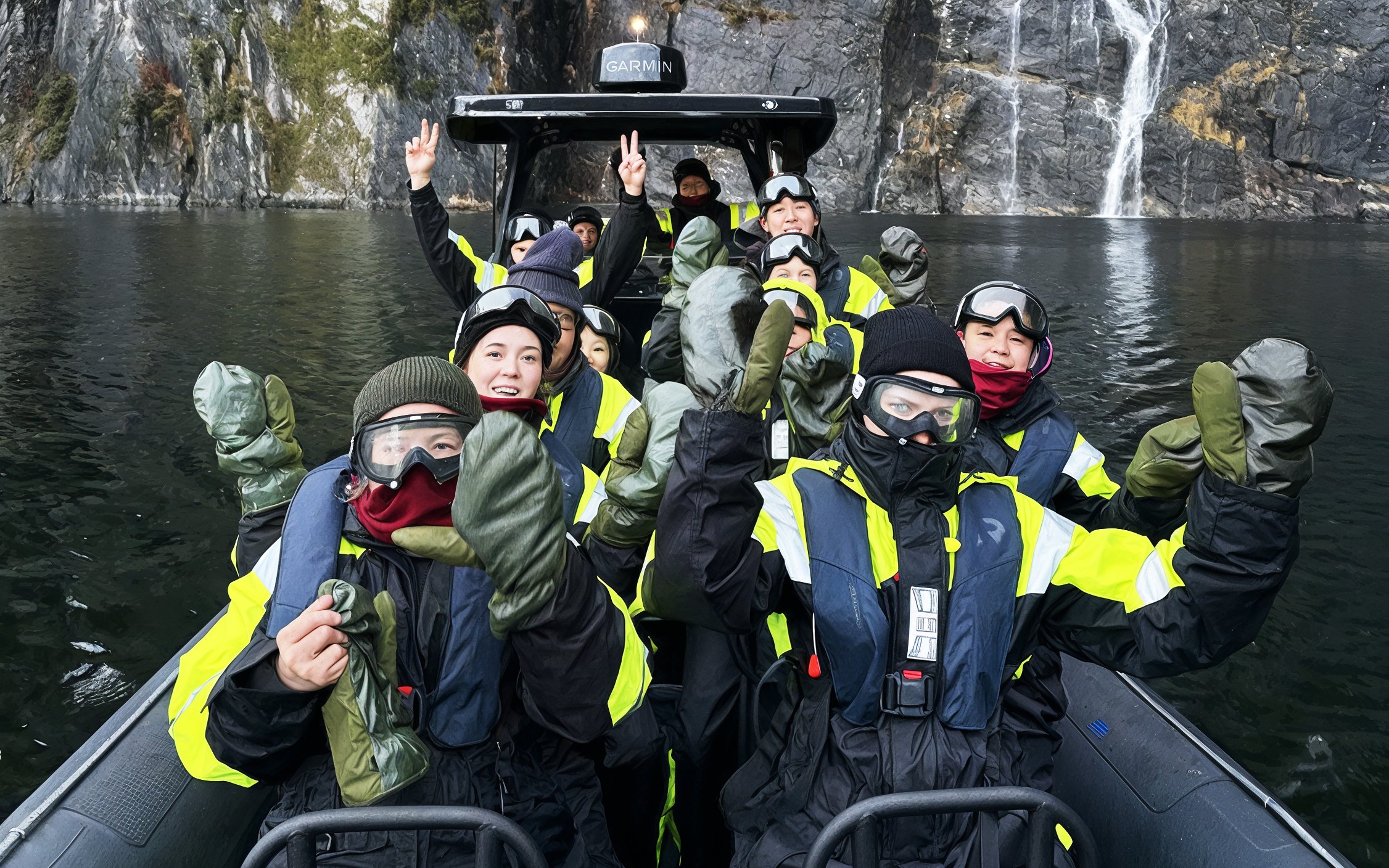 Group in thermal suits and goggles on a boat in a narrow fjord.