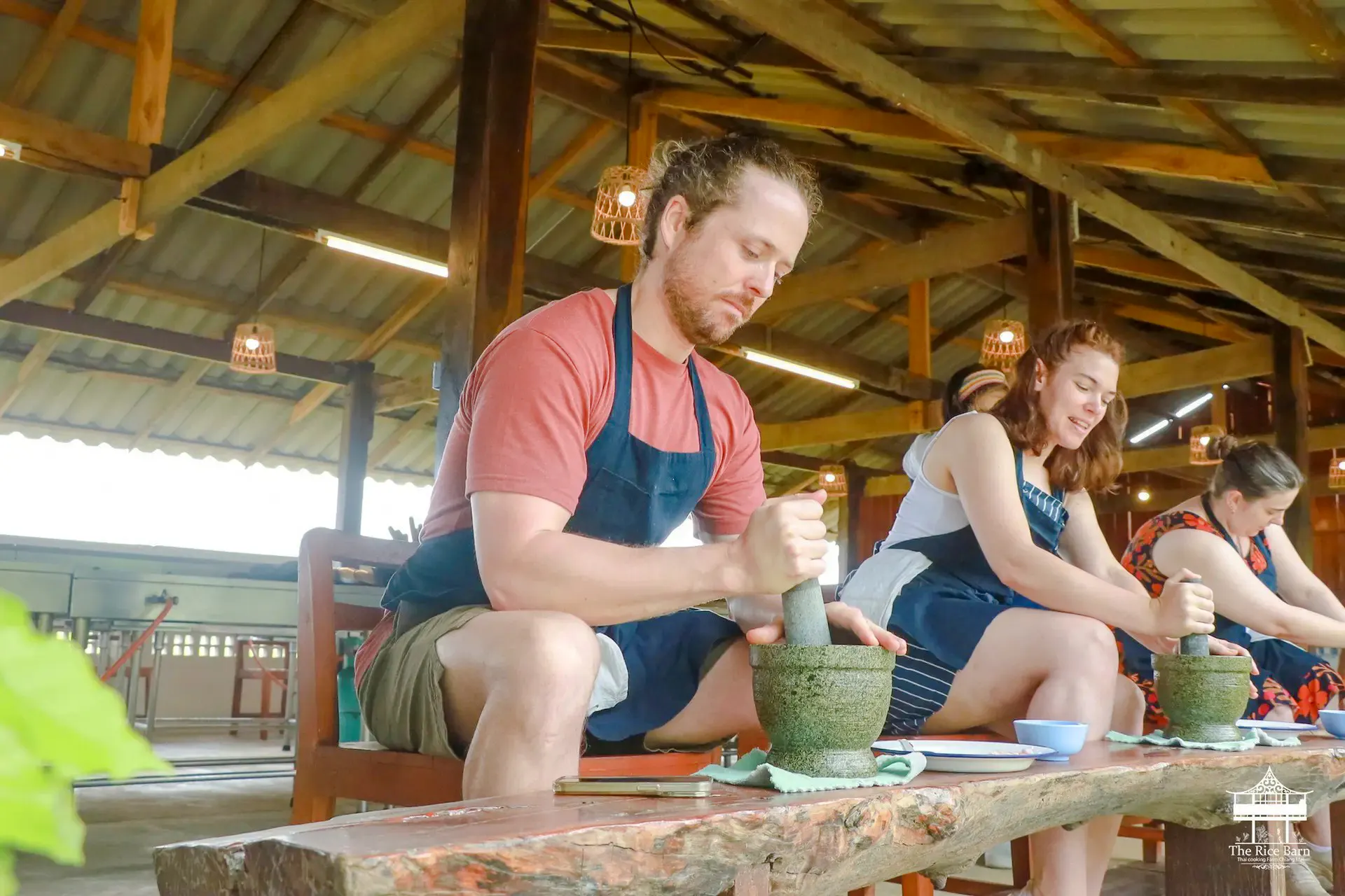People using mortar and pestle at The Rice Barn Thai Cooking Farm, Chiang Mai.