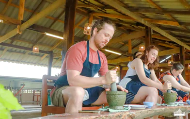 People using mortar and pestle at The Rice Barn Thai Cooking Farm, Chiang Mai.