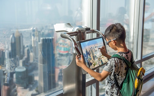Child using electronic telescope at Level 124, Burj Khalifa, viewing Dubai skyline.