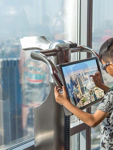 Child using electronic telescope at Level 124, Burj Khalifa, viewing Dubai skyline.