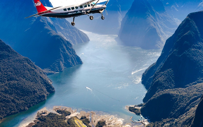Aerial view of Milford Sound with cruise ship and plane, Queenstown scenic flyover experience.