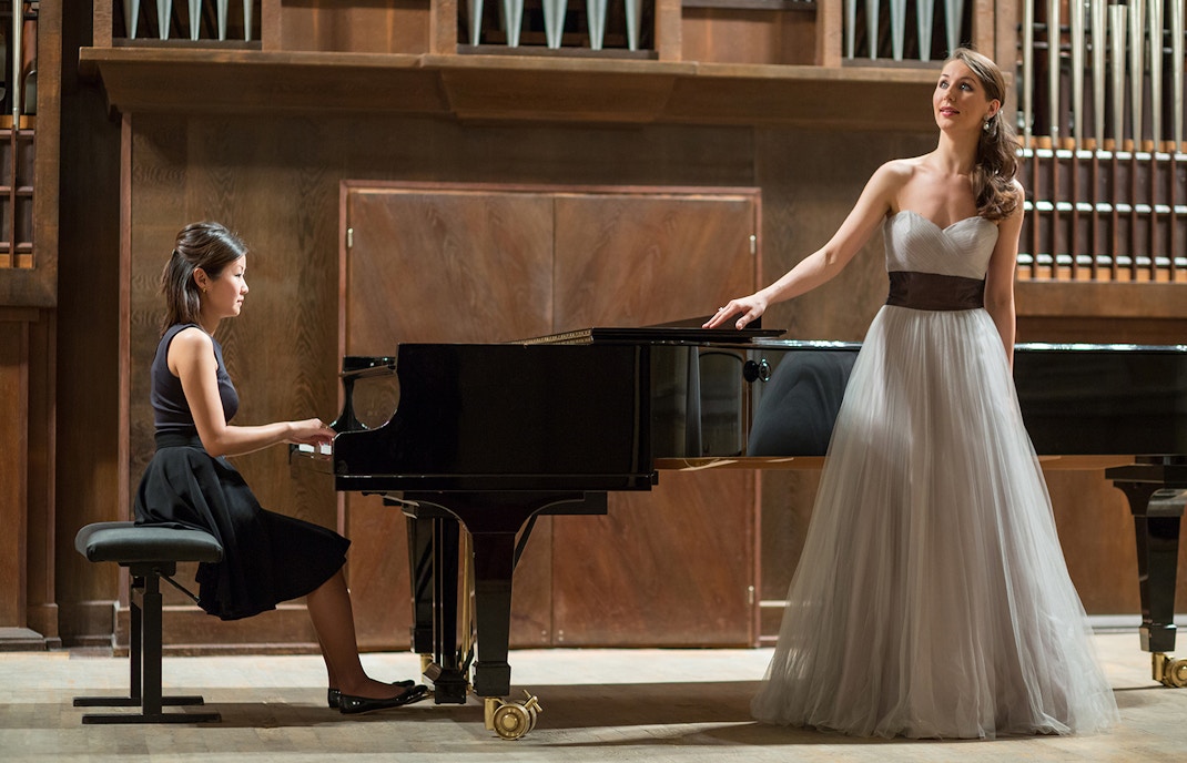 Opera singer performing with pianist in a concert hall.