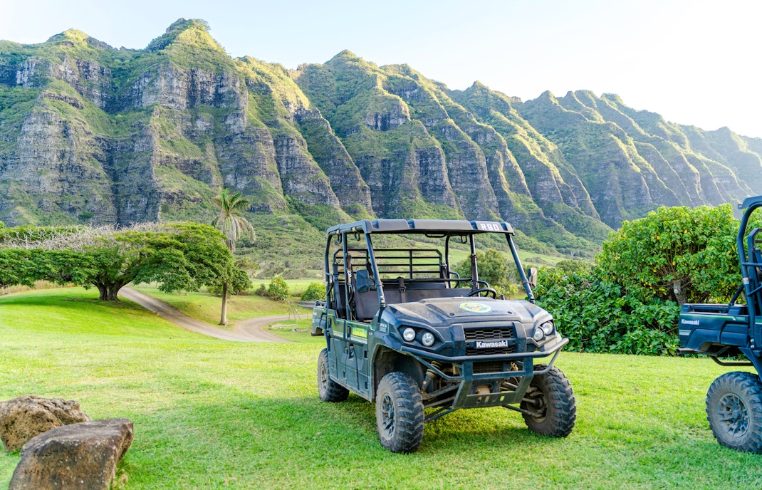 ATV parked on grassy field with Kualoa Ranch mountains in the background.