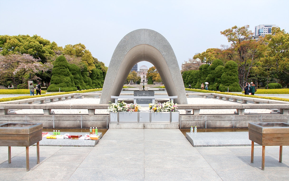 Hiroshima Peace Memorial Park cenotaph with flowers, view of Atomic Bomb Dome in background.