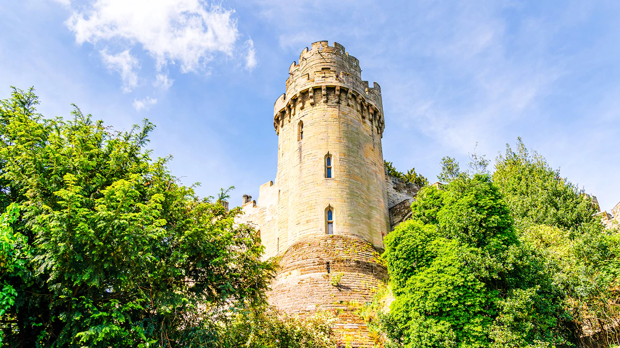 Caesar’s Tower at Warwick Castle surrounded by lush greenery under a clear blue sky.