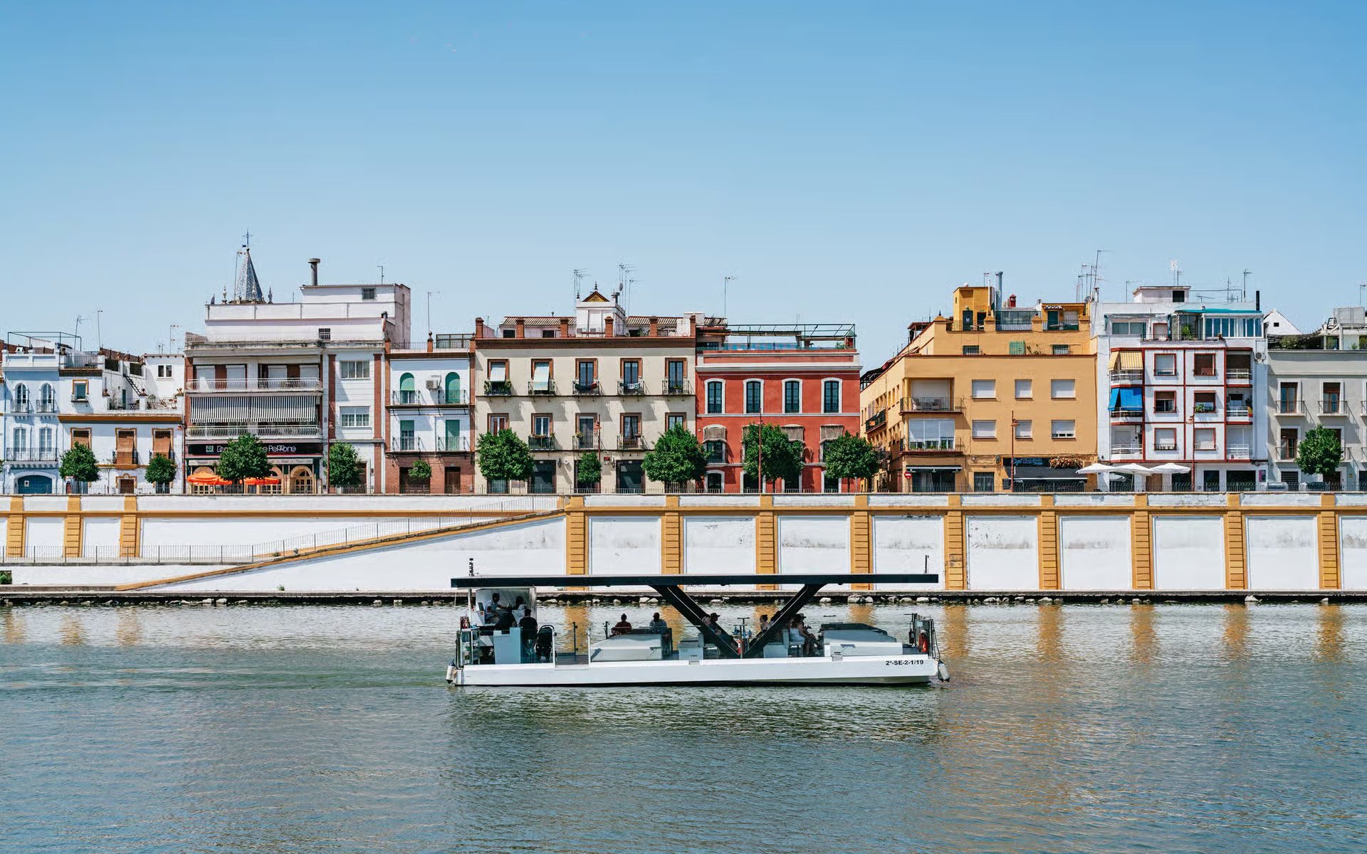 Cruise boat on Guadalquivir River with colorful buildings in Seville, Spain.