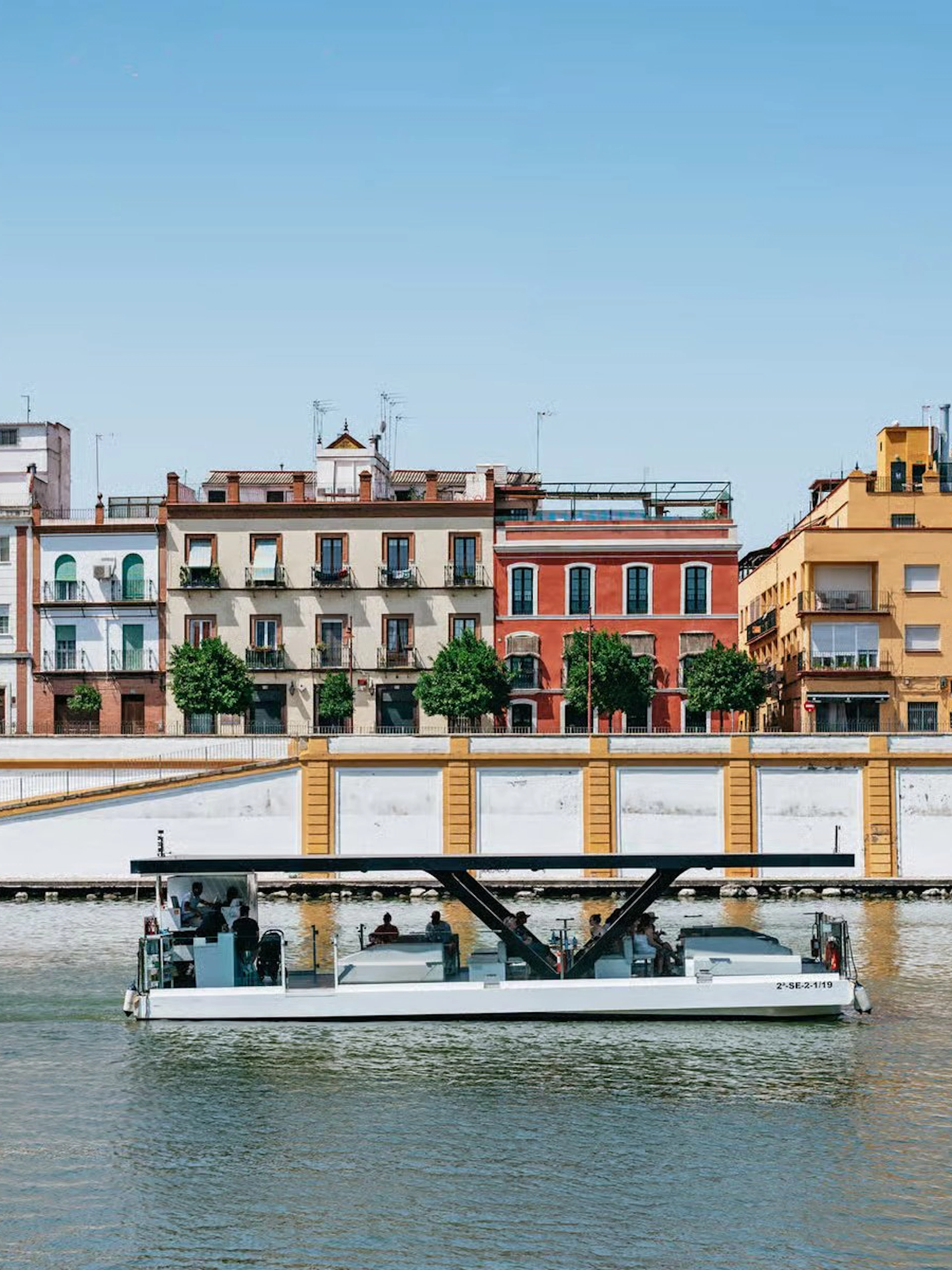Cruise boat on Guadalquivir River with colorful buildings in Seville, Spain.