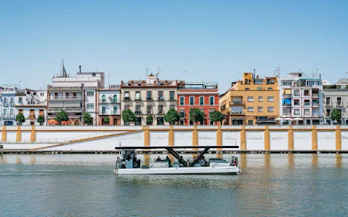 Cruise boat on Guadalquivir River with colorful buildings in Seville, Spain.