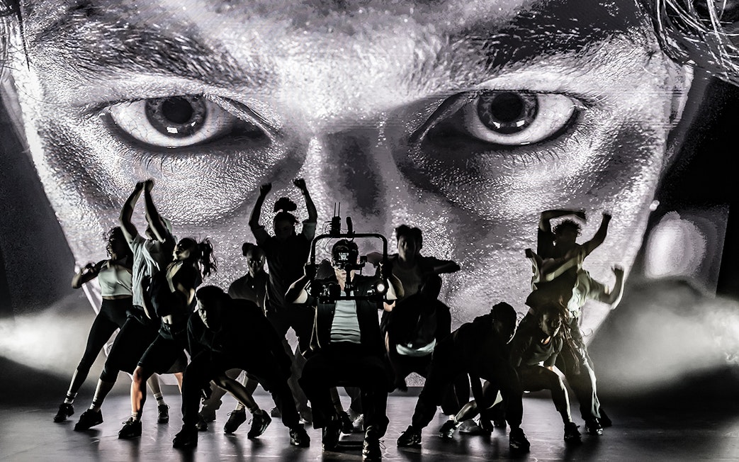 Dancers performing on stage with a large face projected behind them, Sunset Boulevard.