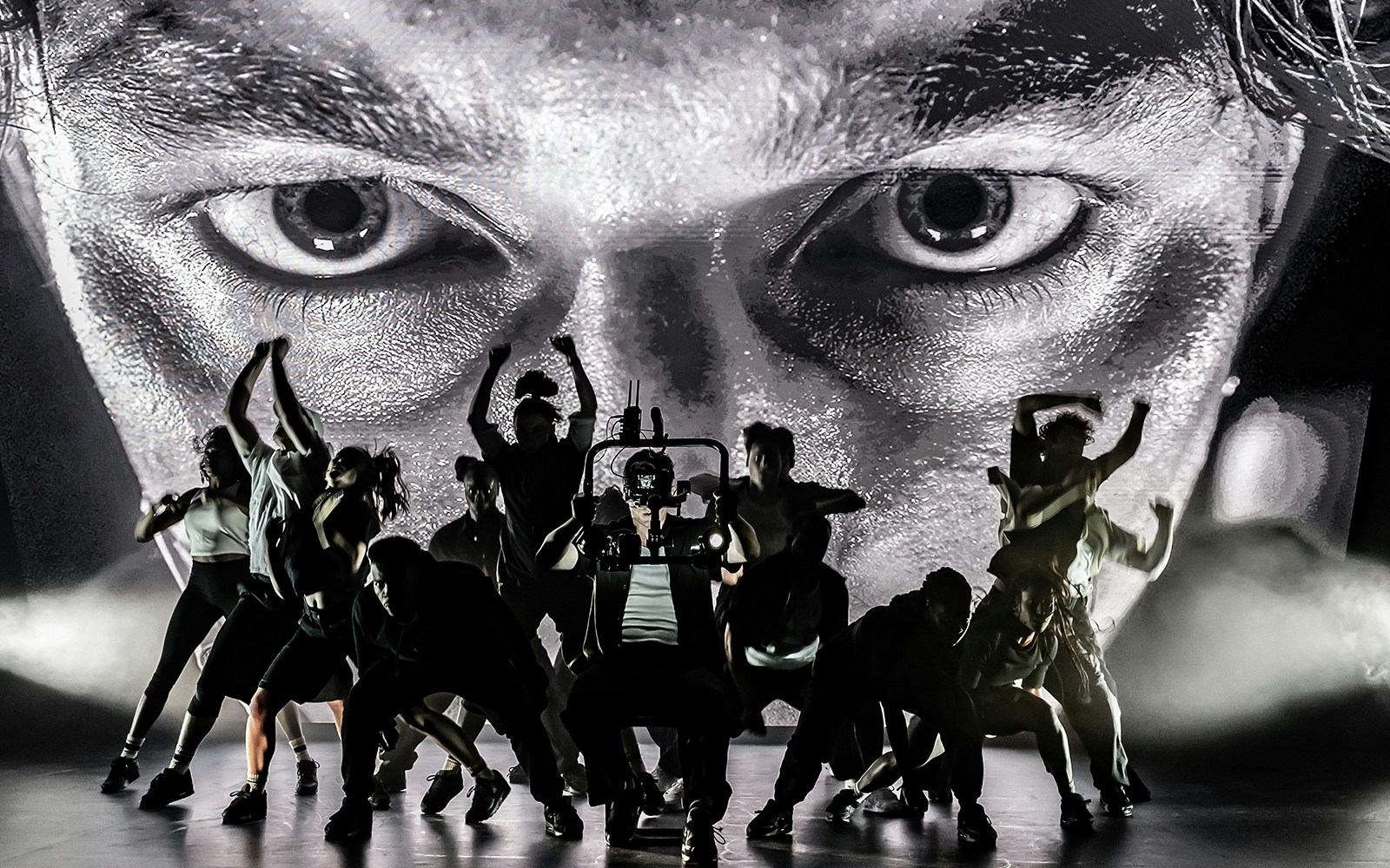 Dancers performing on stage with a large face projected behind them, Sunset Boulevard.