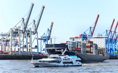 Harbor cruise boat passing container ship and cranes in Hamburg port.