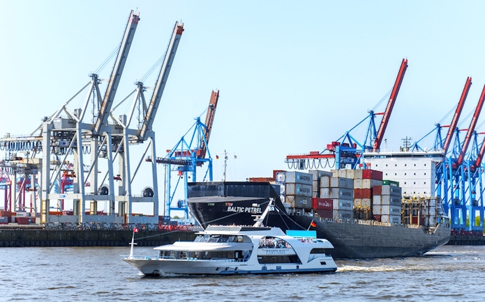 Harbor cruise boat passing container ship and cranes in Hamburg port.