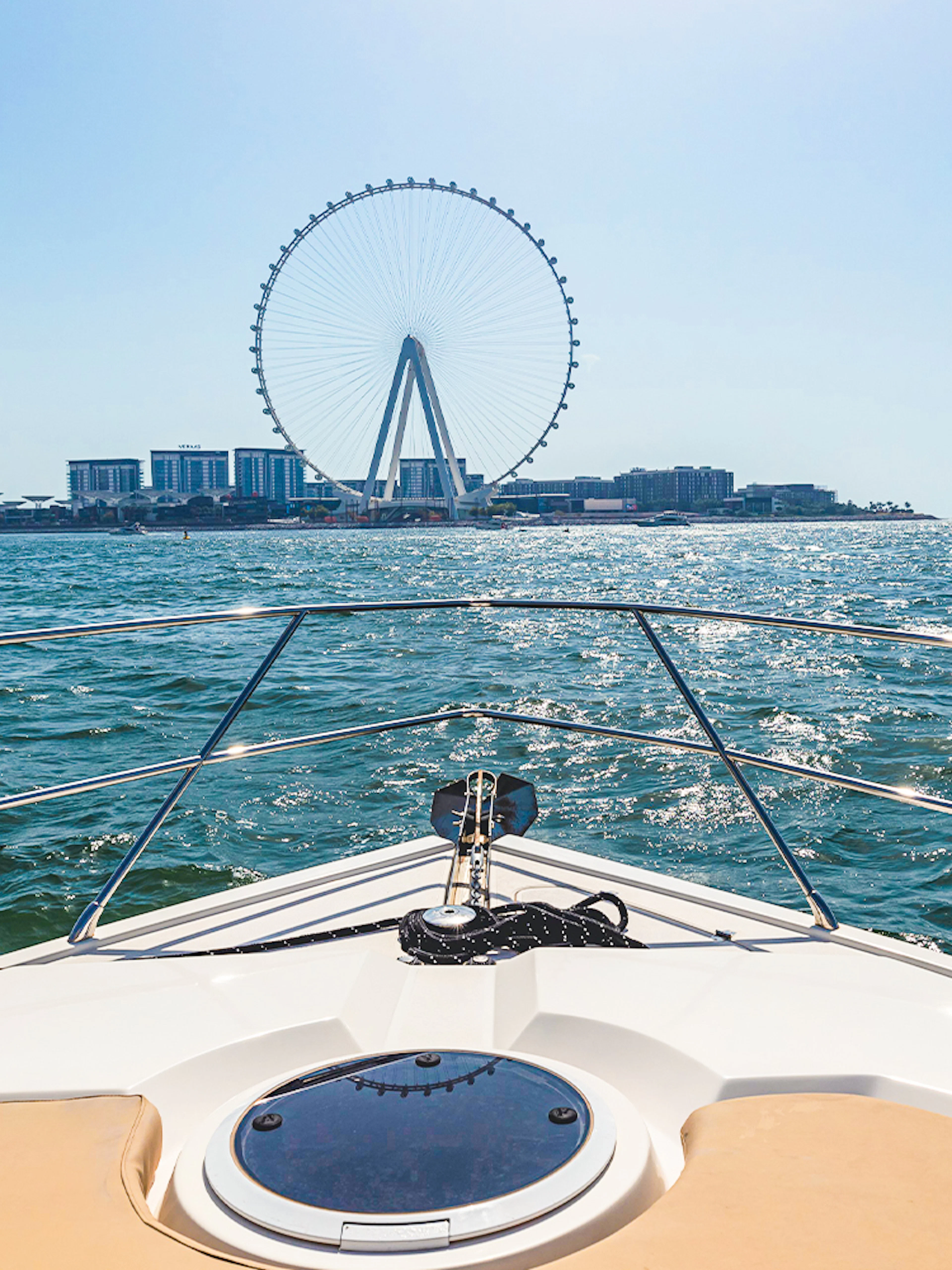 Luxury yacht cruising towards Ain Dubai on a sunny day.