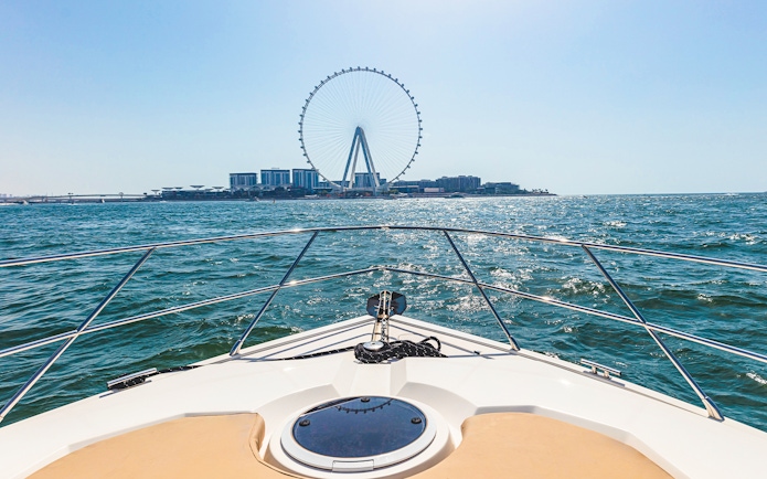Luxury yacht cruising towards Ain Dubai on a sunny day.