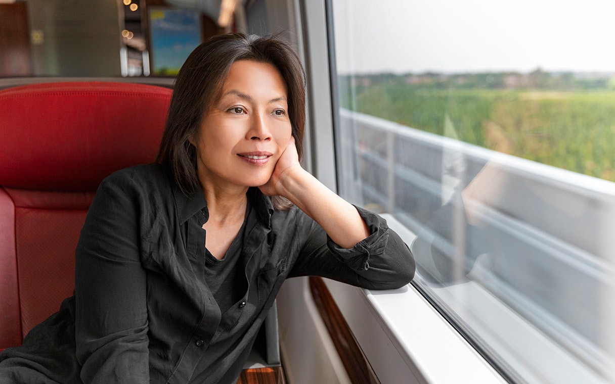 Asian woman gazing out train window at countryside scenery.