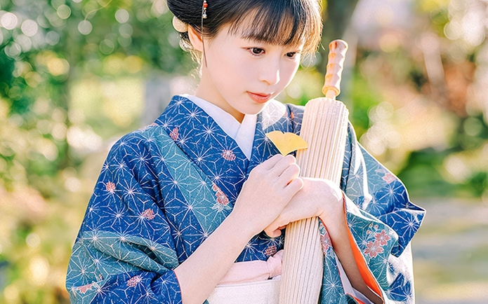 Person in traditional Japanese kimono holding a fan outdoors.