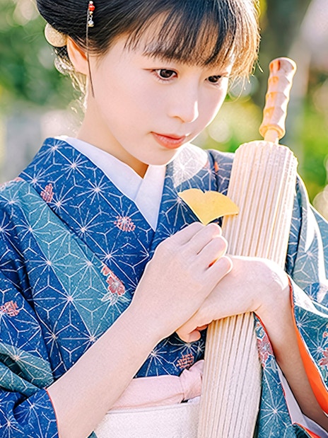 Person in traditional Japanese kimono holding a fan outdoors.