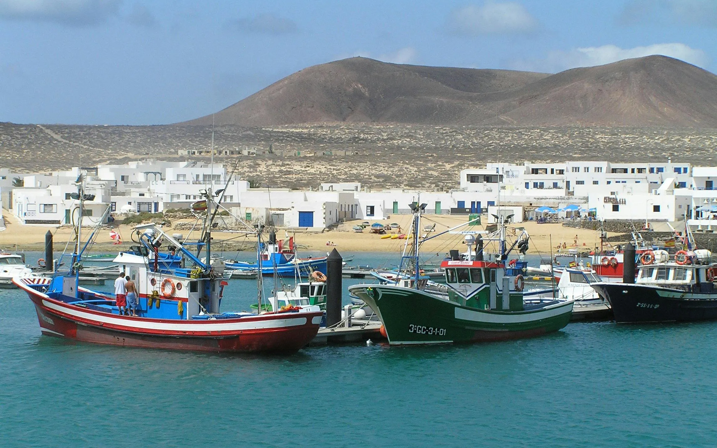 Fishing boats docked at Caleta de Sebo harbor, La Graciosa, Canary Islands, with white buildings and hills in the background.