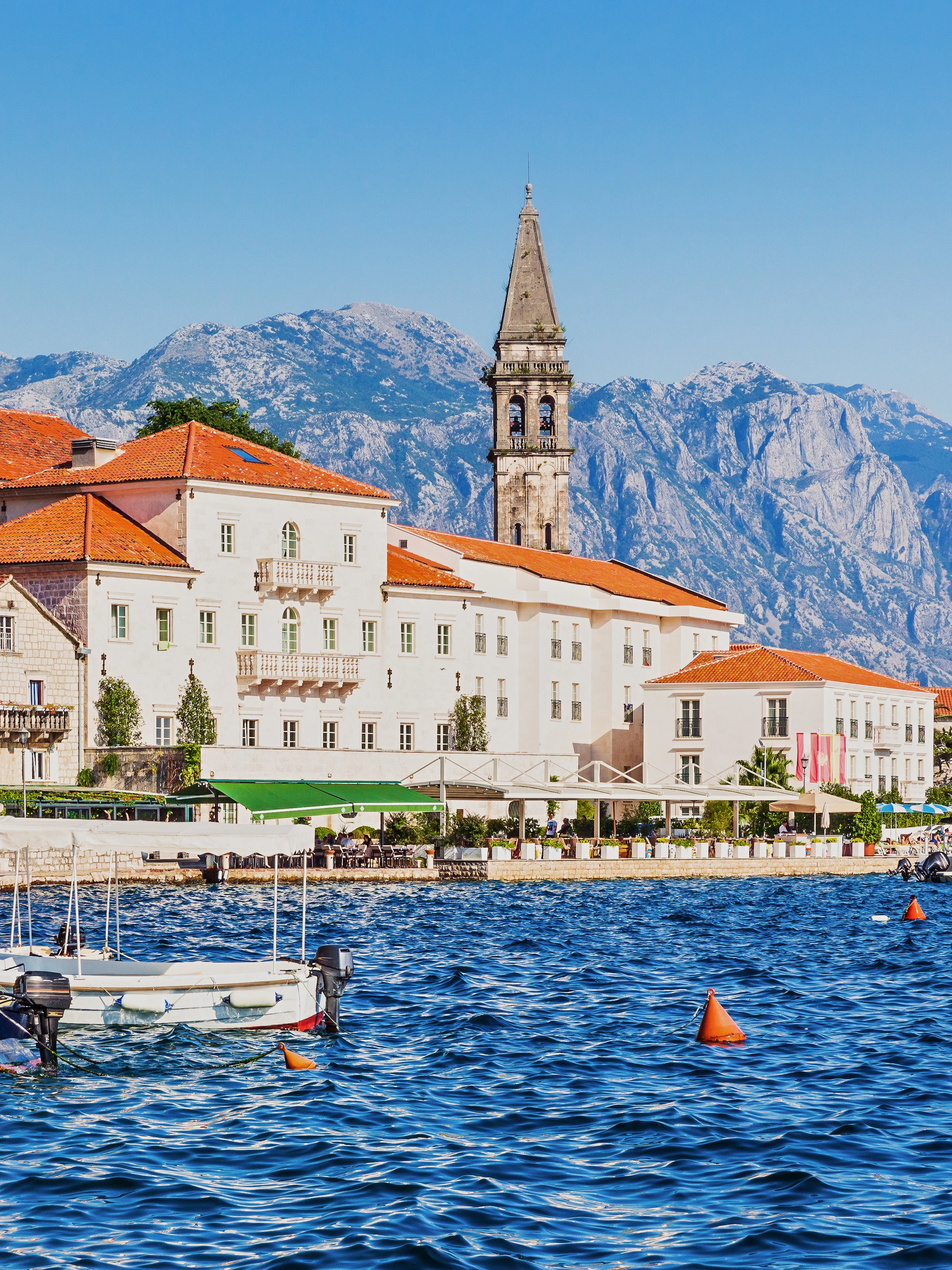Historic waterfront buildings and boats in Perast, Montenegro, with mountains in the background.
