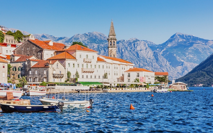 Historic waterfront buildings and boats in Perast, Montenegro, with mountains in the background.
