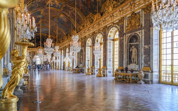 Hall of Mirrors interior at Versailles Palace with chandeliers and statues.