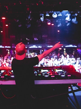 DJ performing at nightclub, view from behind with crowd and lights.