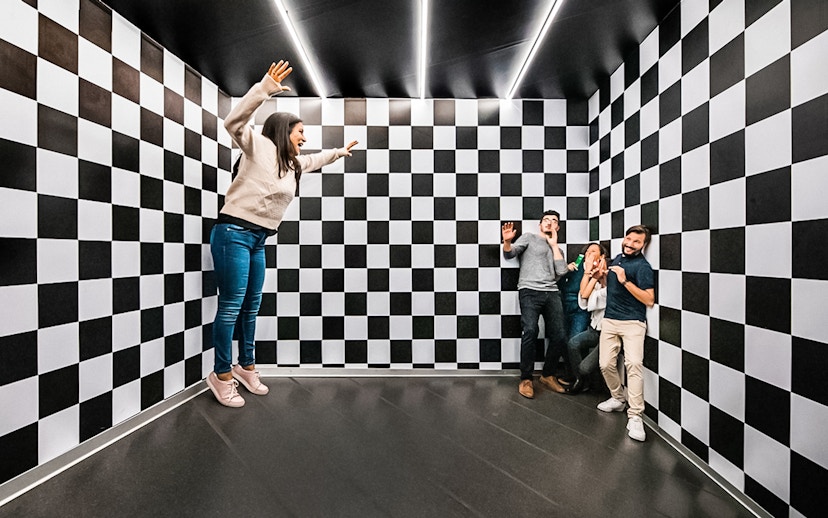 Visitors experiencing optical illusion in the Ames Room at Illuseum Berlin.