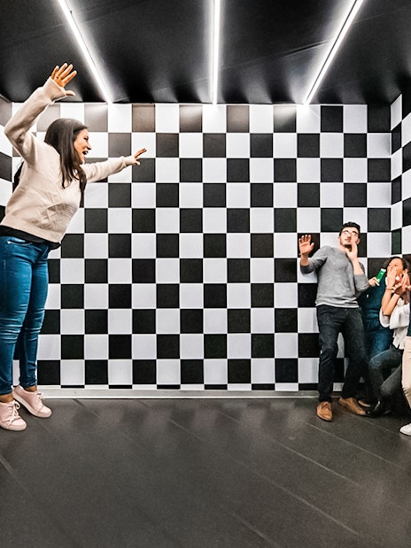 Visitors experiencing optical illusion in the Ames Room at Illuseum Berlin.