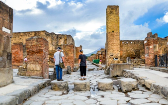Tourists exploring ancient ruins in Pompeii, Italy, with Mount Vesuvius in the background.