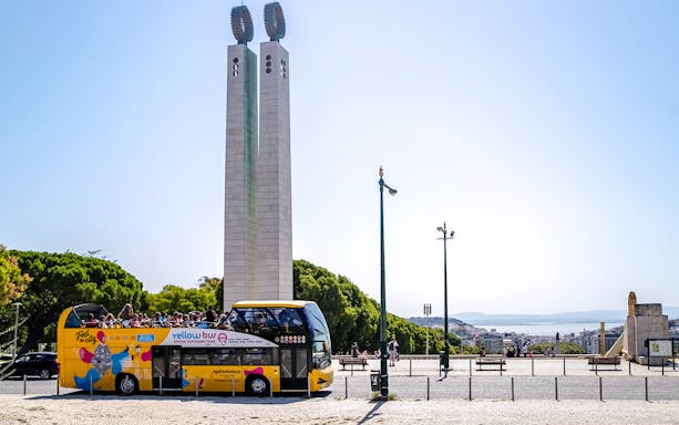 Tourists on a yellow sightseeing bus near Lisbon's Eduardo VII Park monument.