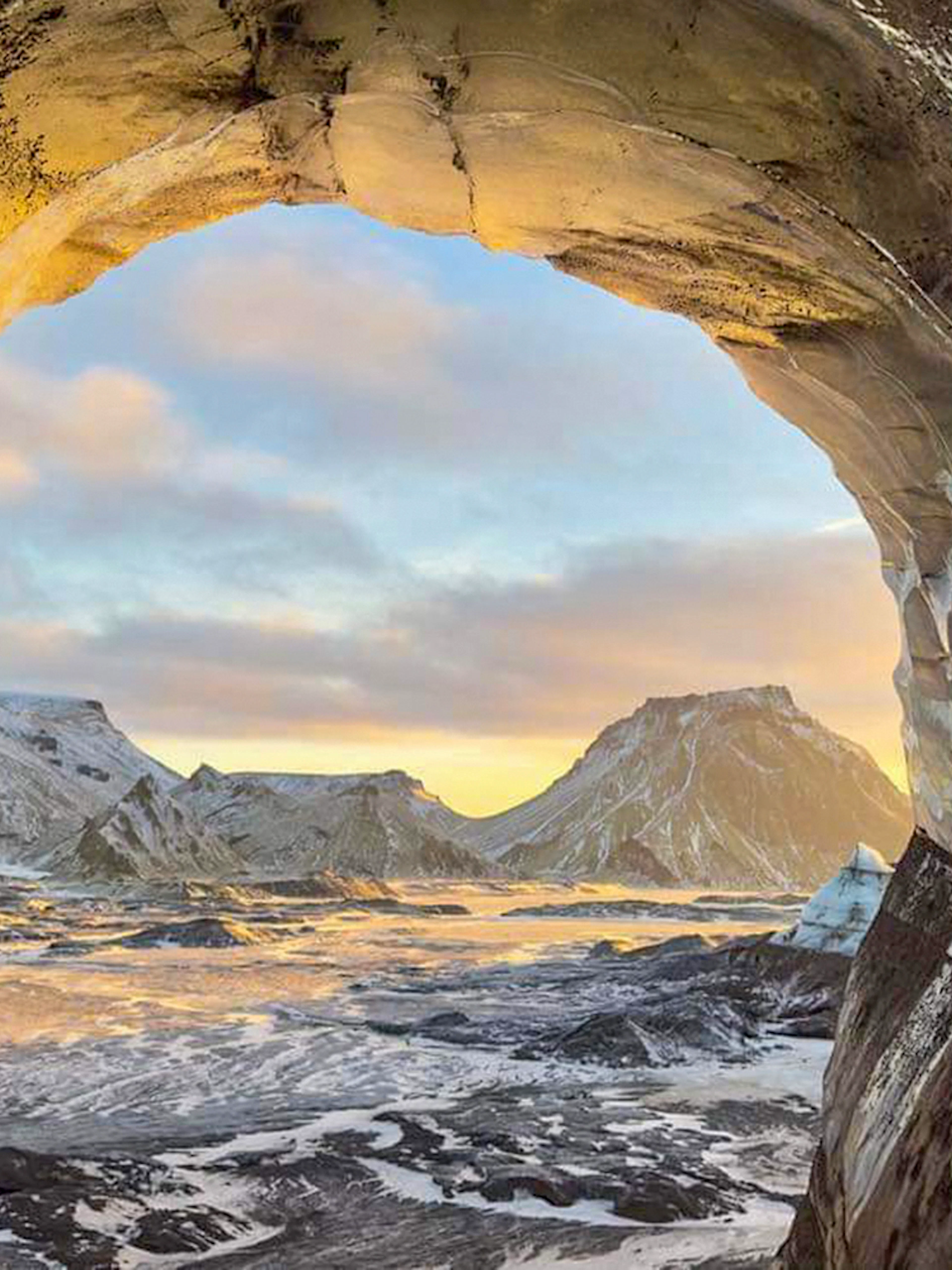 View from inside Katla Ice Cave, Iceland, showing snow-covered mountains and sky.