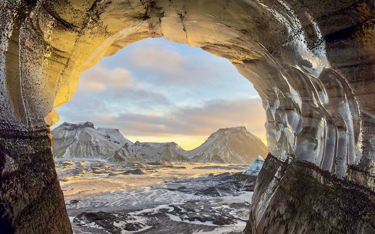View from inside Katla Ice Cave, Iceland, showing snow-covered mountains and sky.