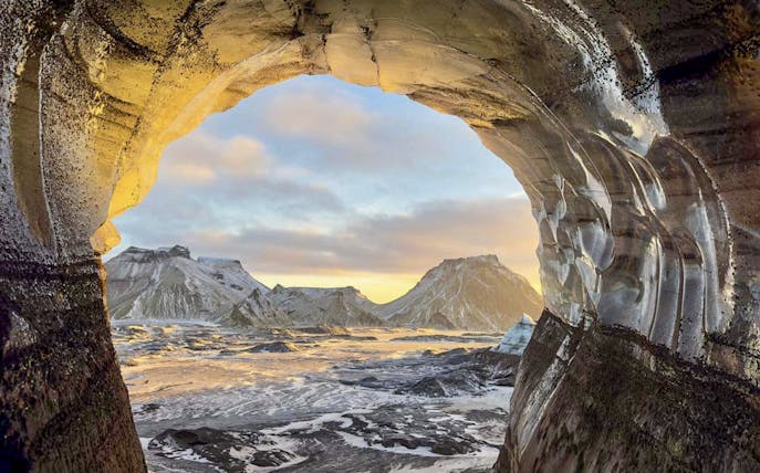 View from inside Katla Ice Cave, Iceland, showing snow-covered mountains and sky.