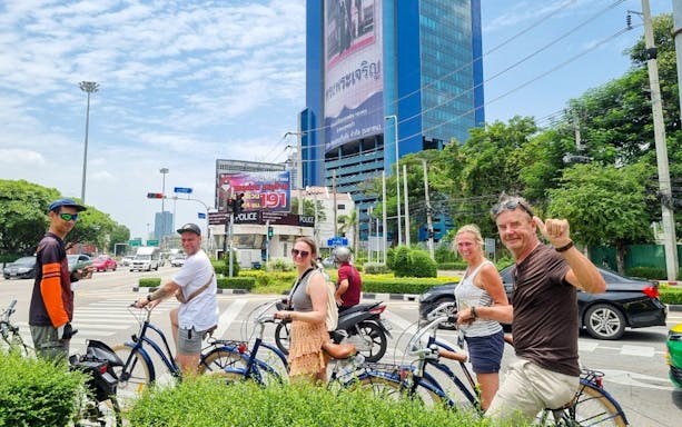 Tourists on bicycles exploring Bangkok city streets with a large building in the background.