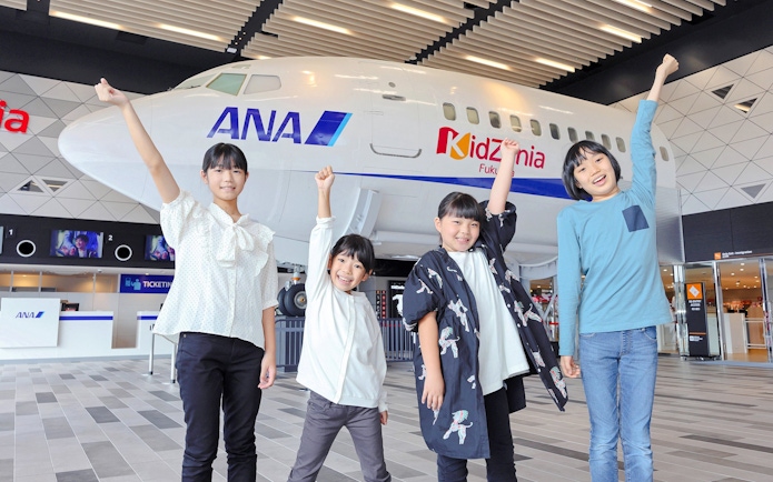 Children posing as aircraft crew at KidZania Fukuoka with an ANA airplane model.