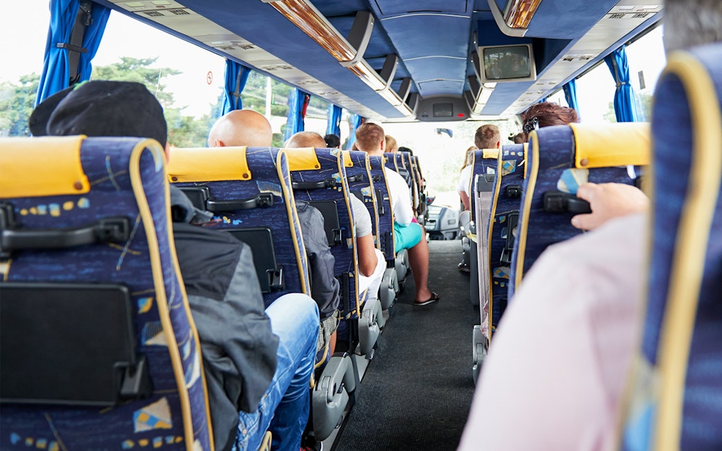 Passengers seated on a tour bus with blue and yellow seats.