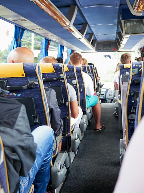 Passengers seated on a tour bus with blue and yellow seats.