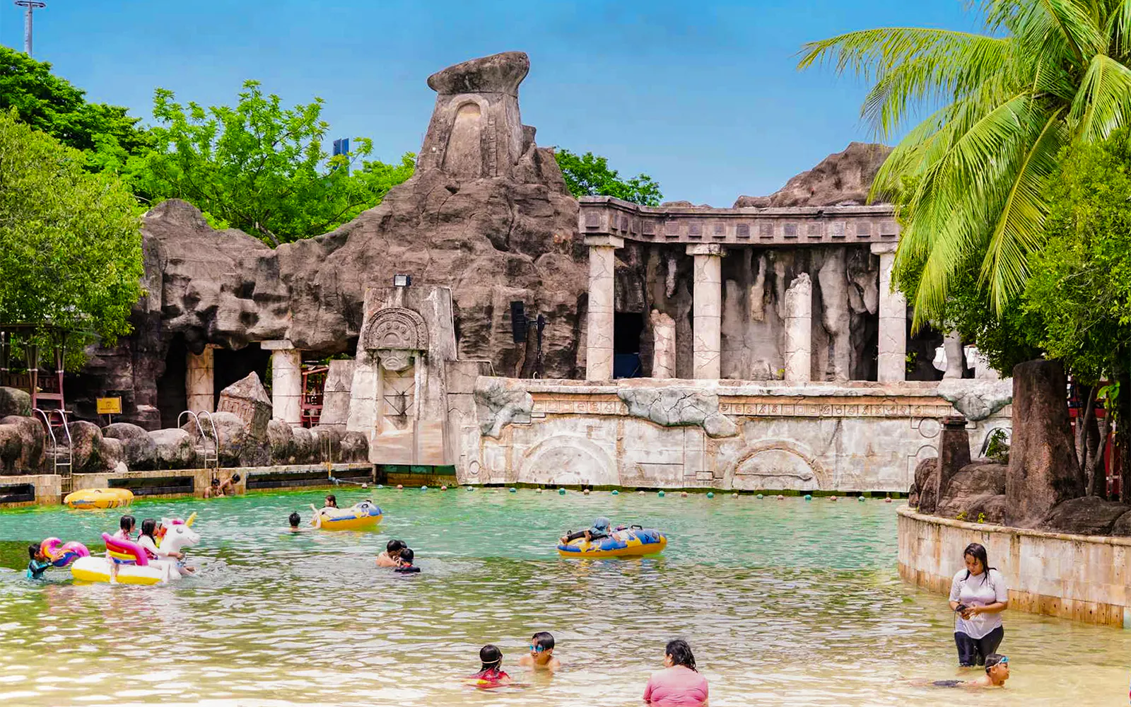 Visitors enjoying the pool at Ancol Atlantis Water Adventure Park, featuring ancient Mediterranean-themed architecture.