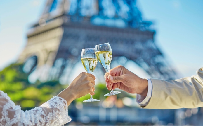 Toasting champagne glasses with Eiffel Tower in background on Seine River cruise.