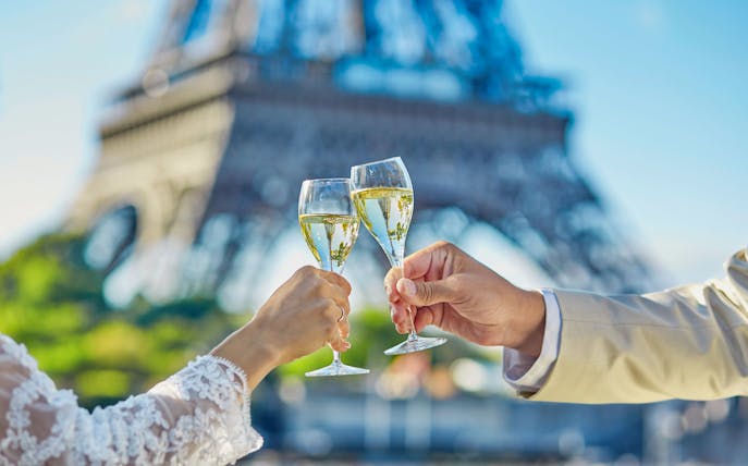 Toasting champagne glasses with Eiffel Tower in background on Seine River cruise.