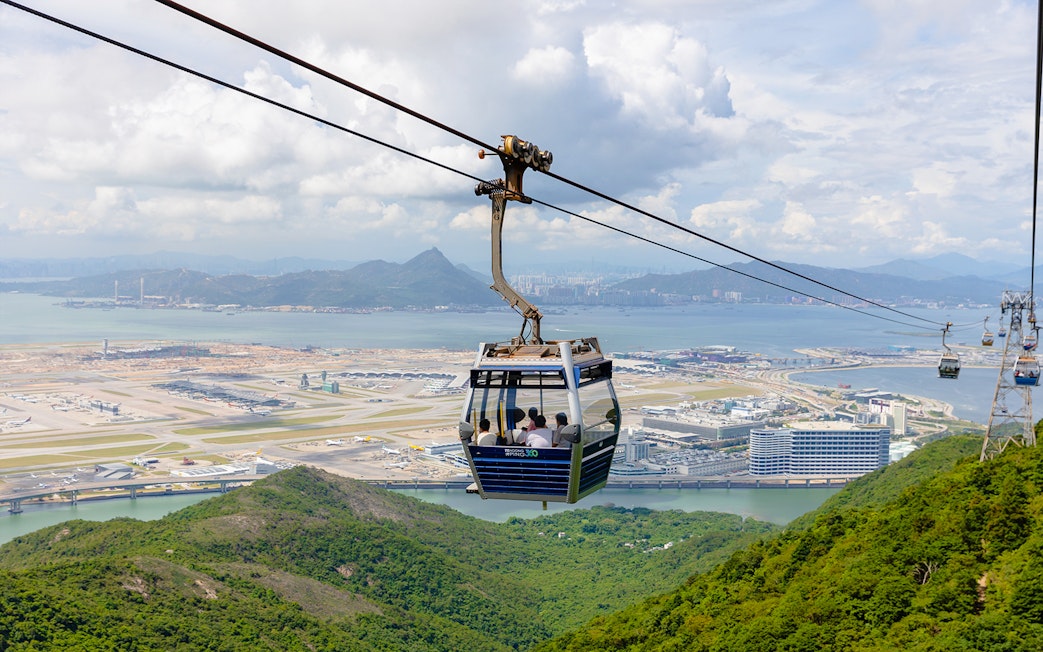 Cable car over lush hills with Hong Kong International Airport in the background at Ngong Ping.