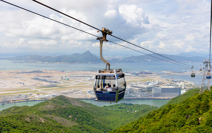 Cable car over lush hills with Hong Kong International Airport in the background at Ngong Ping.