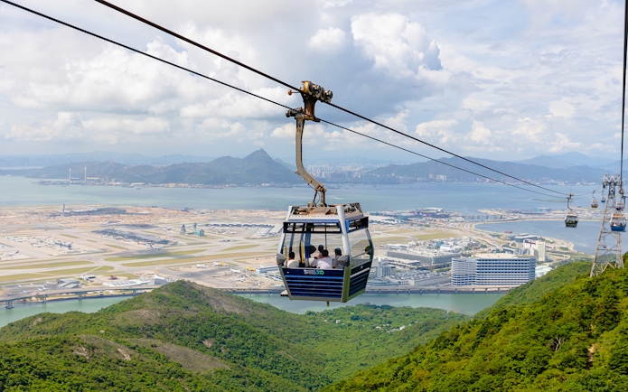 Cable car over lush hills with Hong Kong International Airport in the background at Ngong Ping.