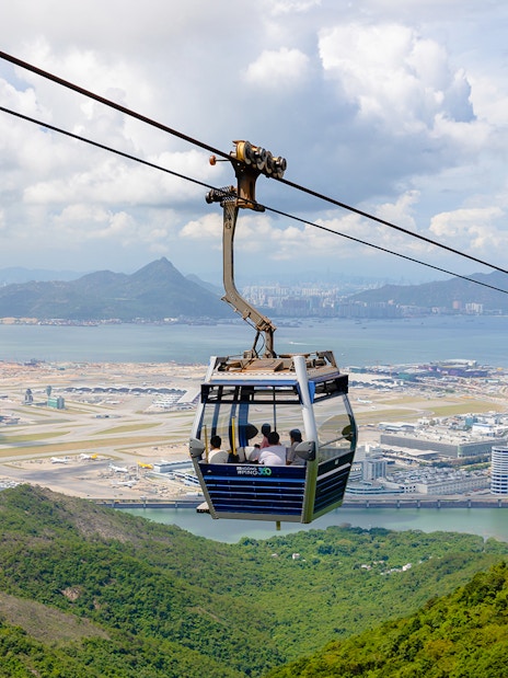 Cable car over lush hills with Hong Kong International Airport in the background at Ngong Ping.
