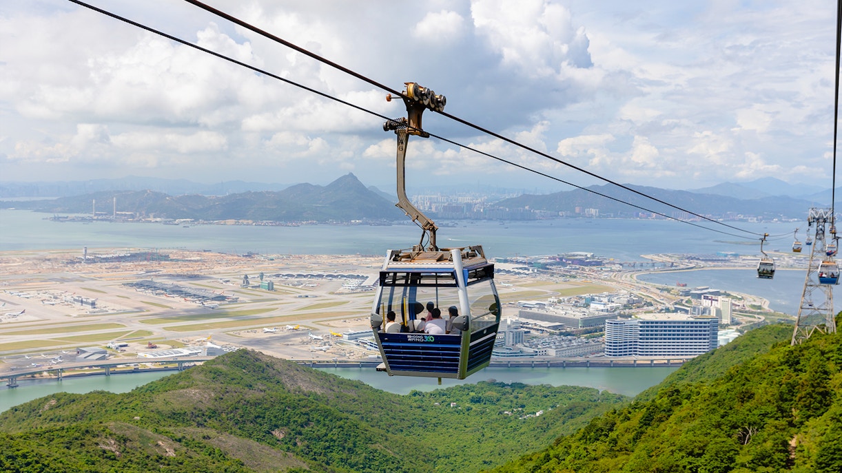 Cable car over lush hills with Hong Kong International Airport in the background at Ngong Ping.