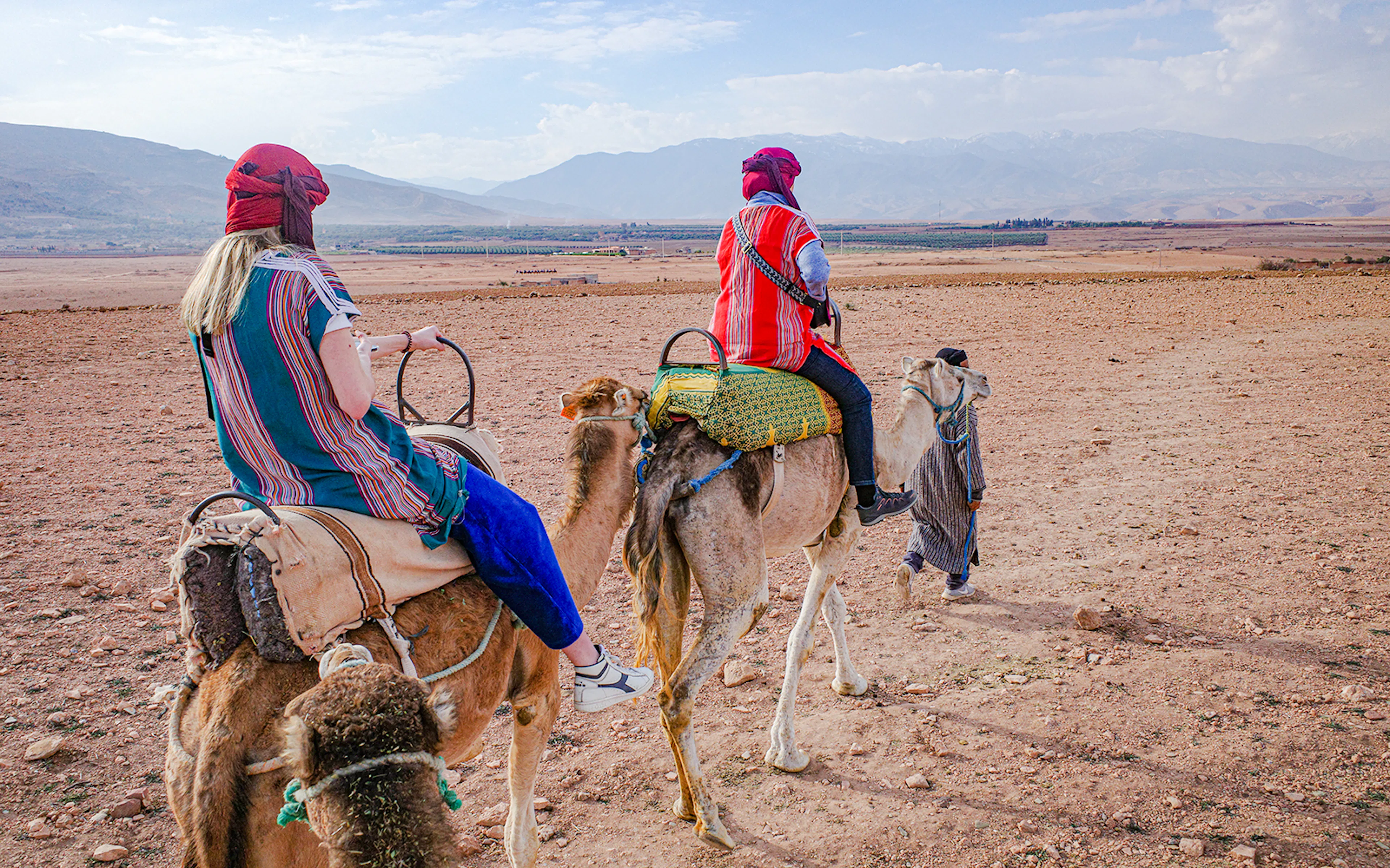 People riding camels in Agafay Desert, Morocco with mountains in the background.