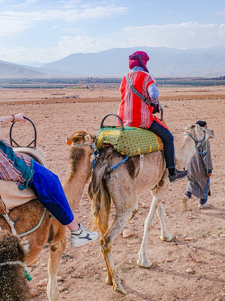 People riding camels in Agafay Desert, Morocco with mountains in the background.